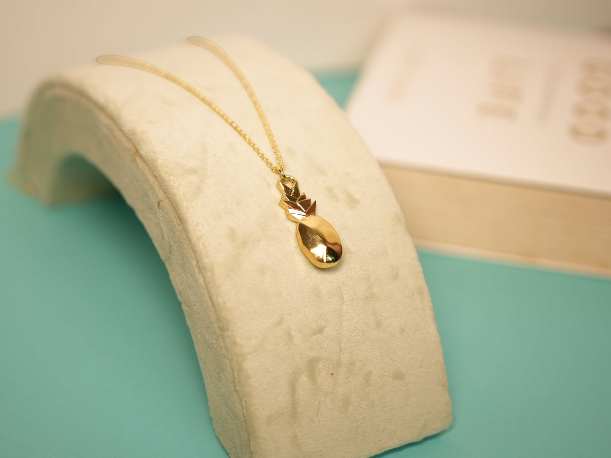 Daga-accessories gold-tone dainty pineapple pendant necklace on a beige display stand
