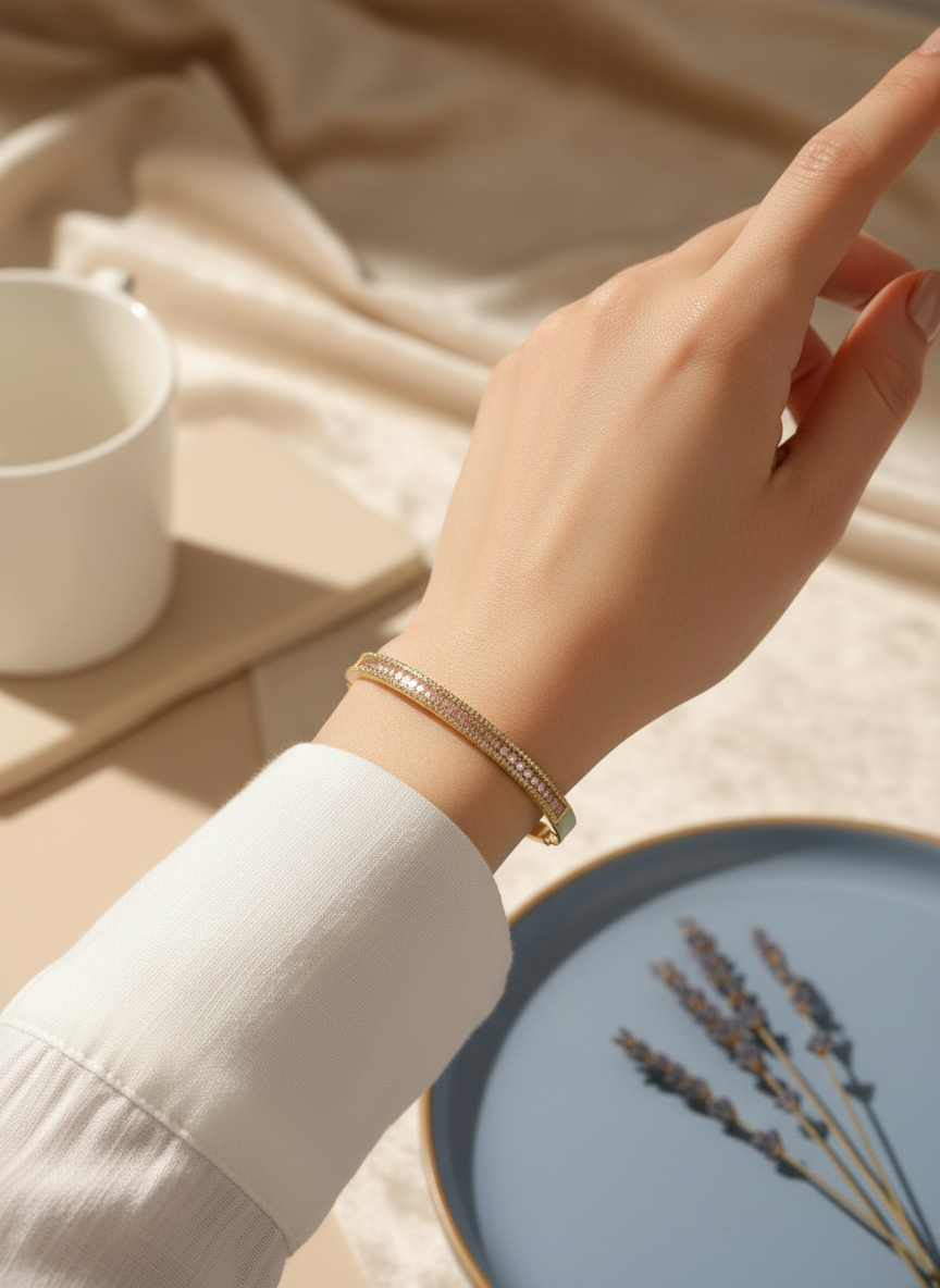 Daga-accessories gold-tone hinged bangle bracelet featuring a row of shimmering pink crystals on a woman's wrist.