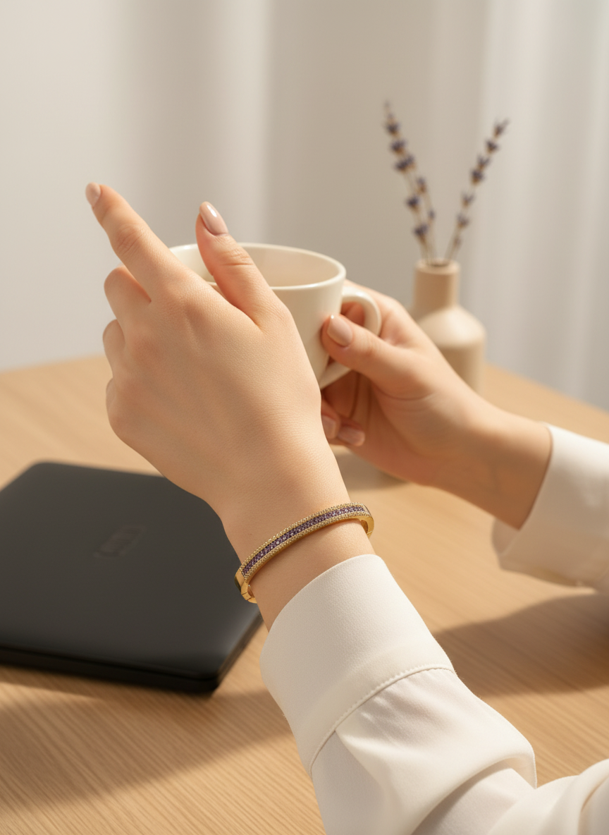 Daga-accessories gold-tone hinged bangle with purple and clear crystals worn on a woman's wrist at a desk