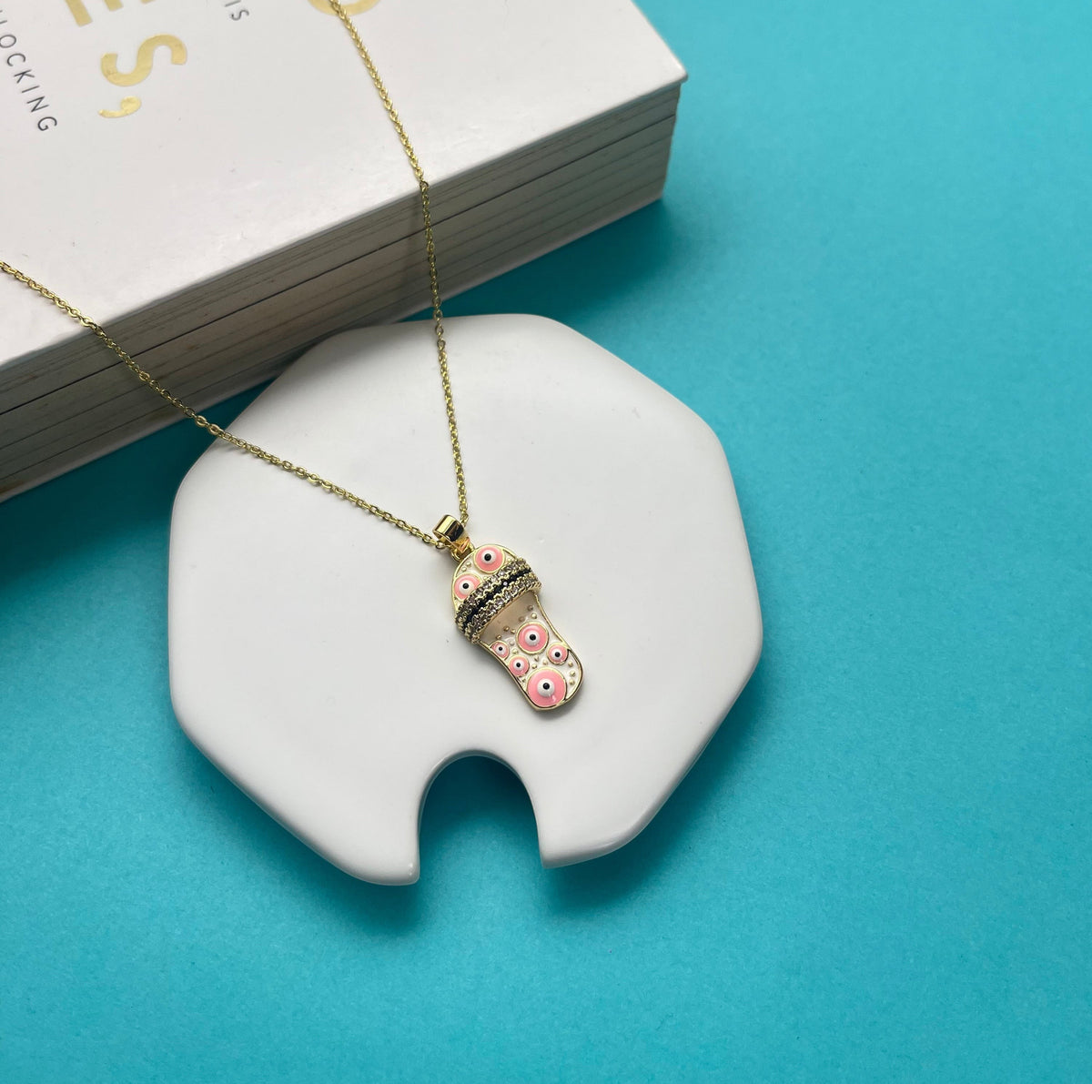 Daga-accessories gold chain necklace with a pink sandal pendant featuring evil eye motifs on a white display stand