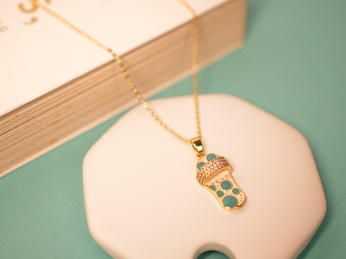 Daga-accessories gold necklace featuring a dainty sandal pendant with blue enamel details and sparkling crystals.