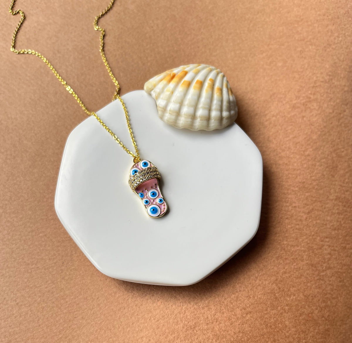 Daga-accessories Glided Footprint Blushy Necklace featuring a gold chain and sandal pendant with blue evil eye beads.