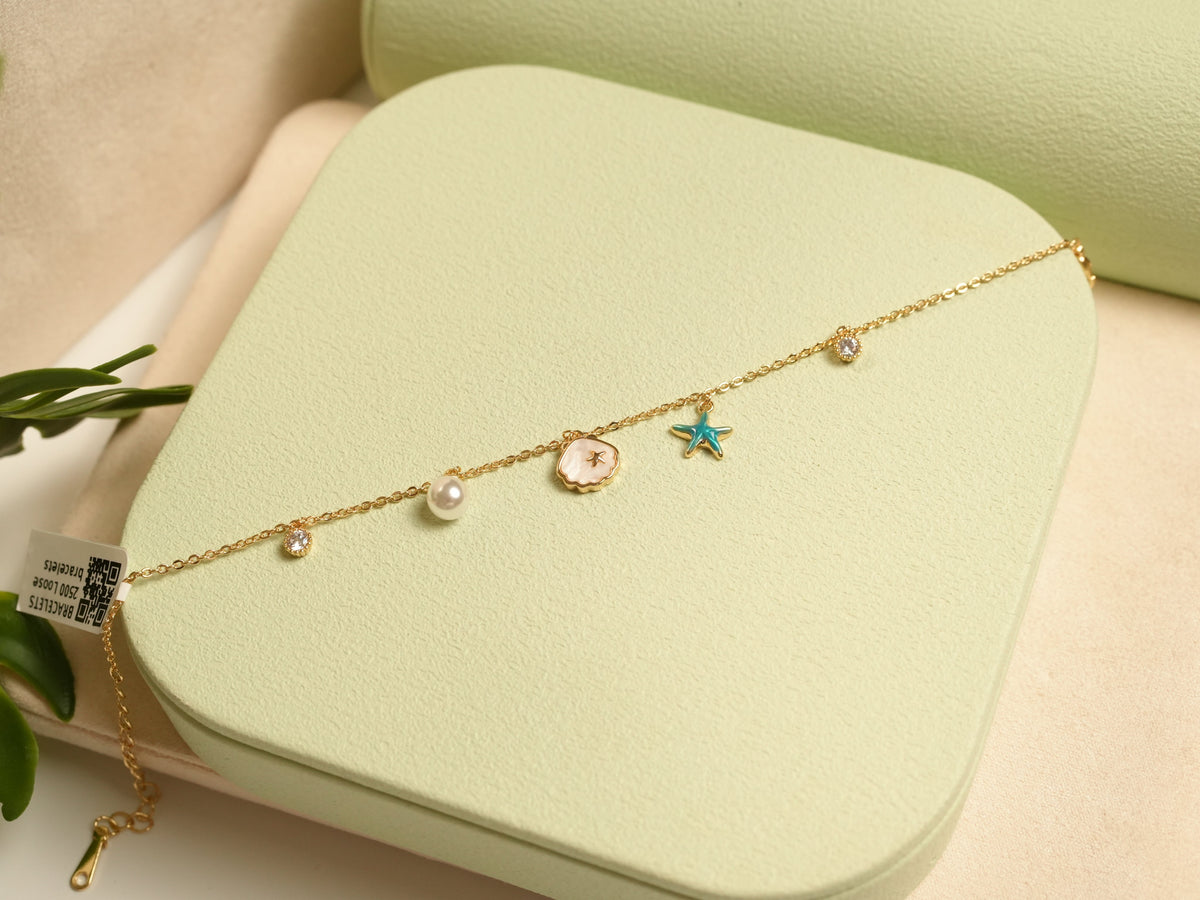 Daga-accessories gold charm bracelet featuring a pearl, shell, and blue starfish charm on a delicate chain.