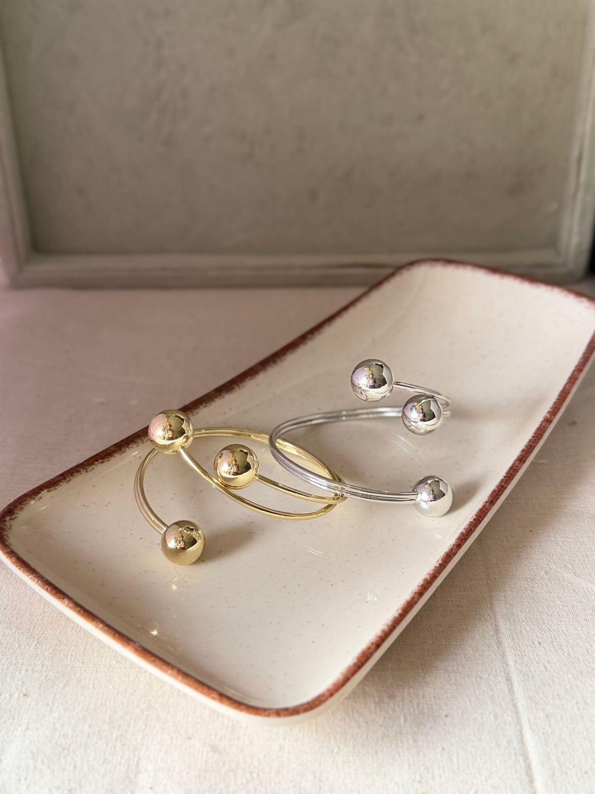 Daga-accessories open cuff bracelets with polished gold and silver spherical accents on a ceramic tray