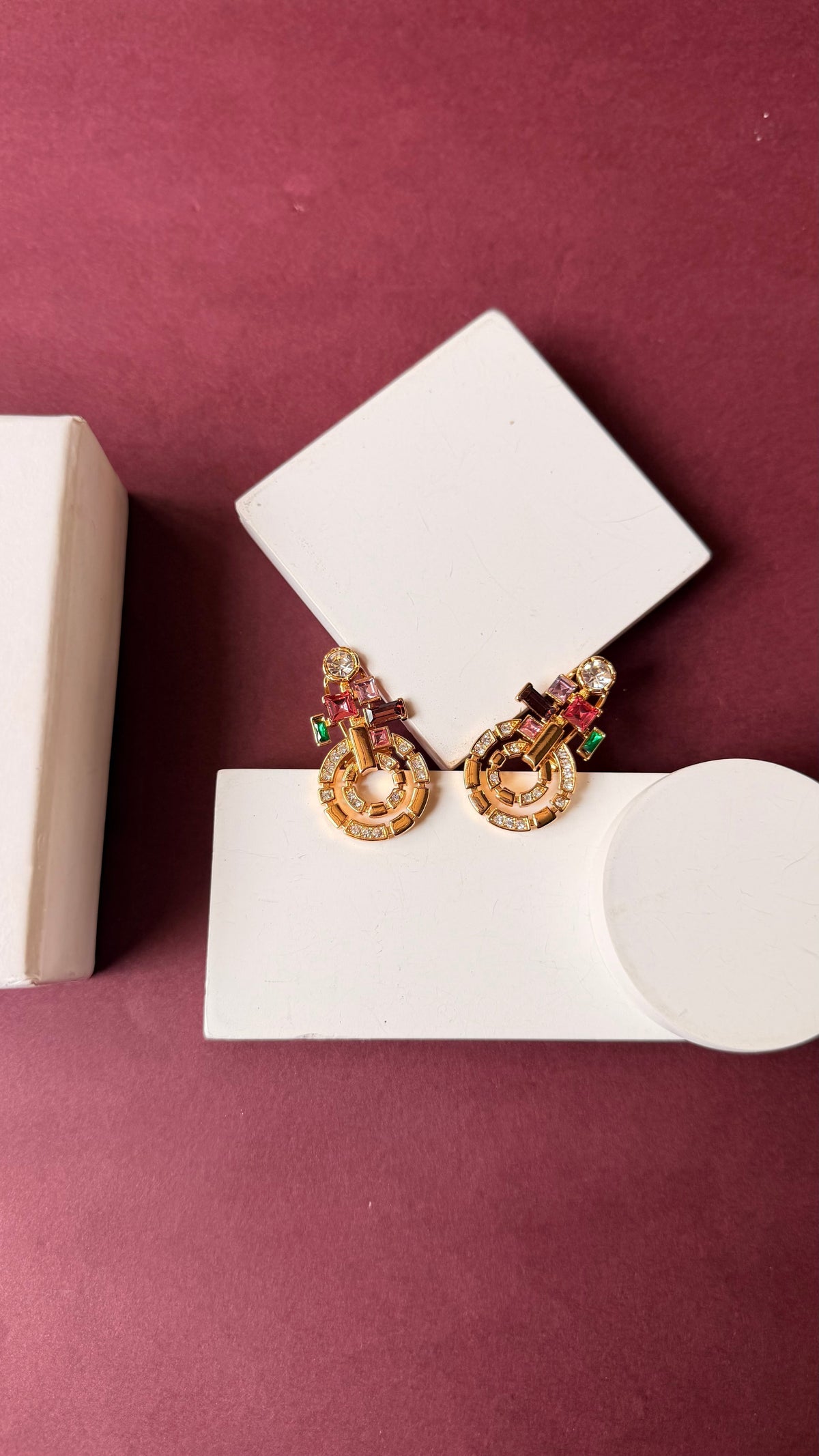 Daga-accessories gold spiral statement earrings with multi-coloured baguette crystals on a maroon background