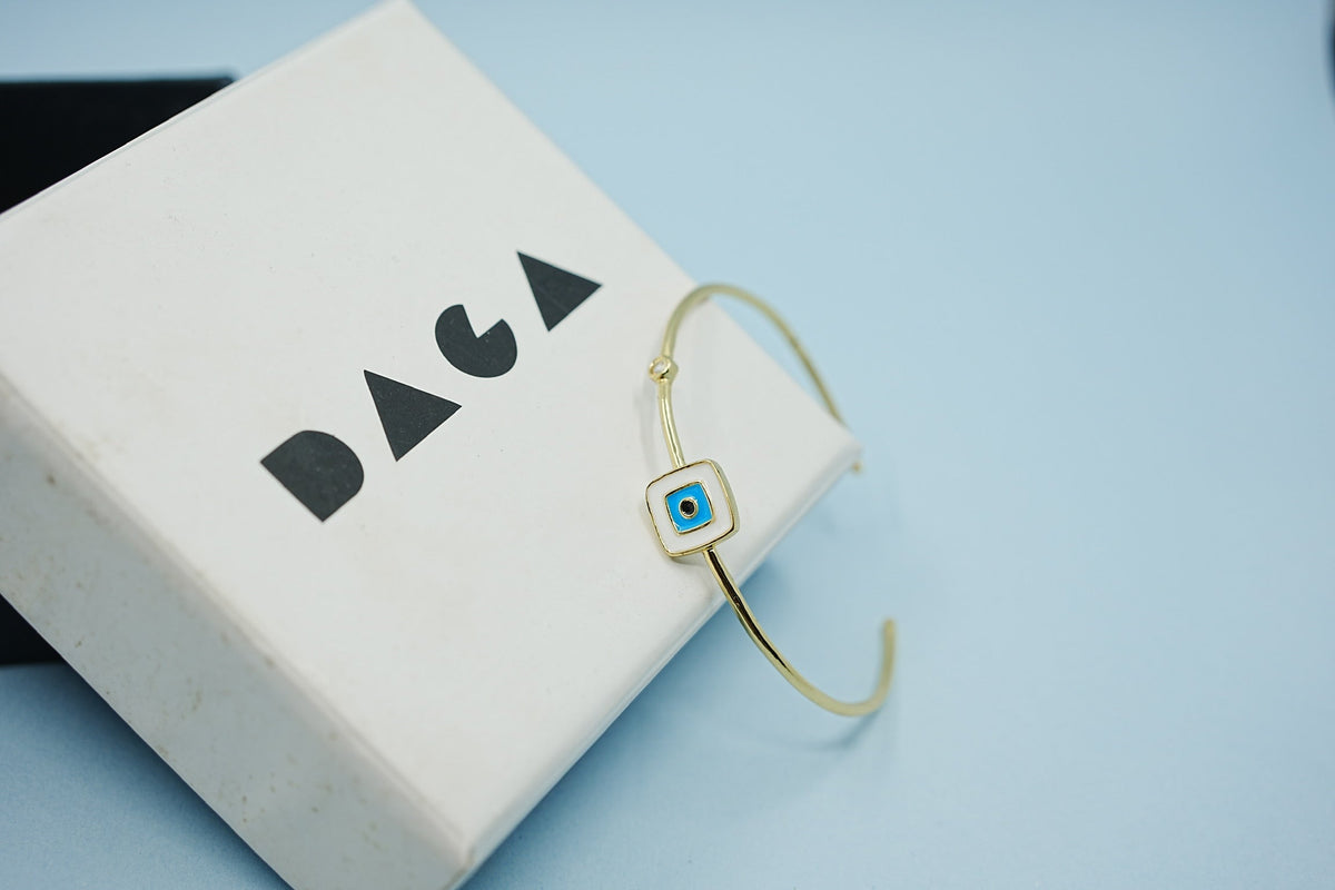 Daga-accessories gold-tone stainless steel cuff bracelet featuring a square white and blue enamel evil eye charm.