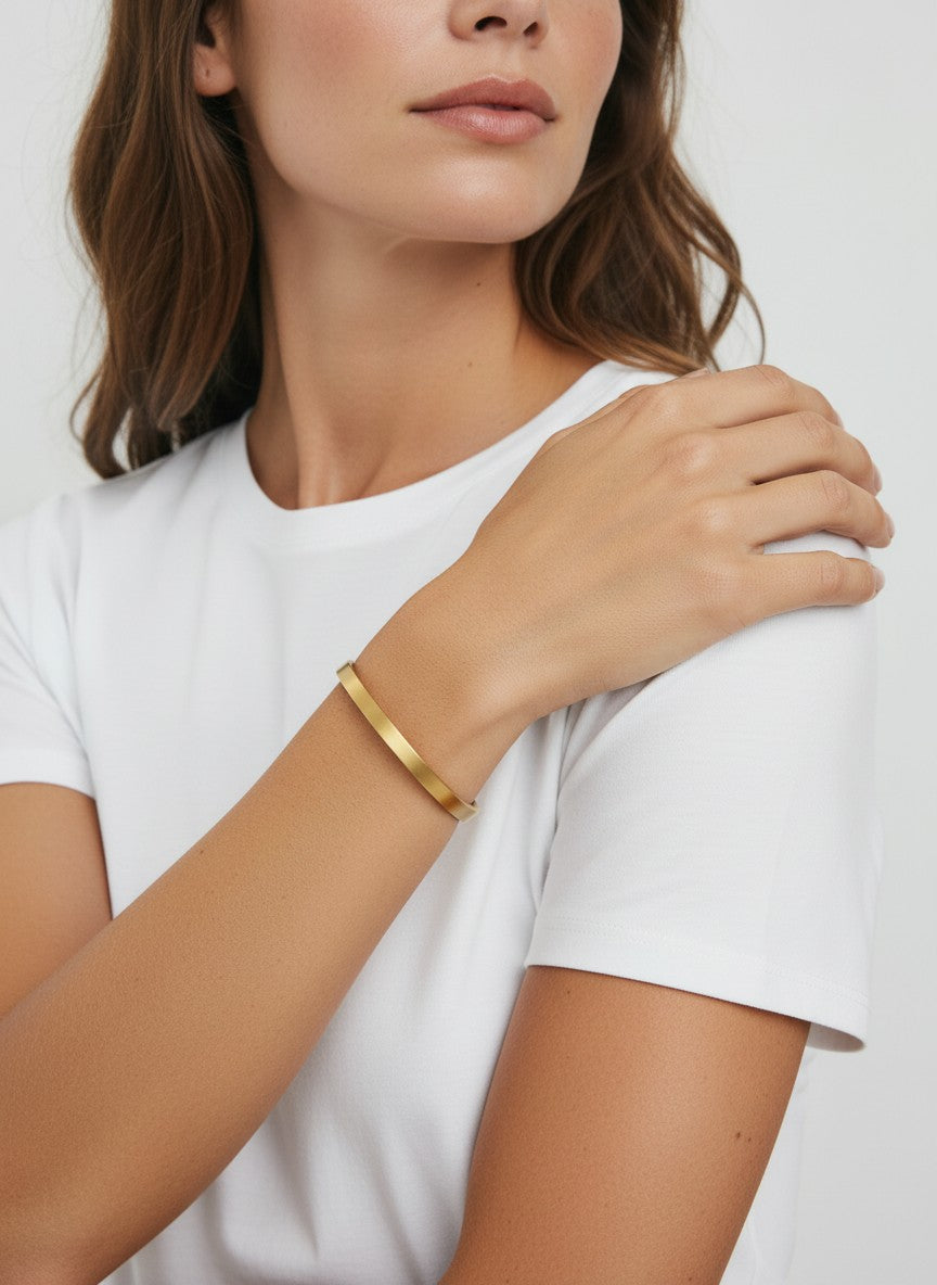 Daga-accessories minimalist gold-toned stainless steel bangle bracelet worn on a woman's wrist with a white t-shirt.