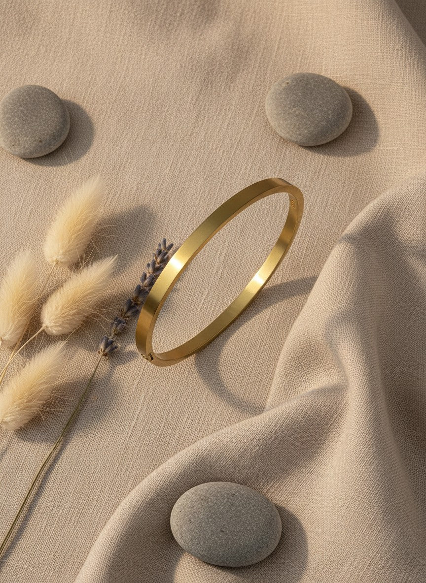 Daga-accessories minimalist gold-toned stainless steel bangle bracelet on a beige fabric background with stones