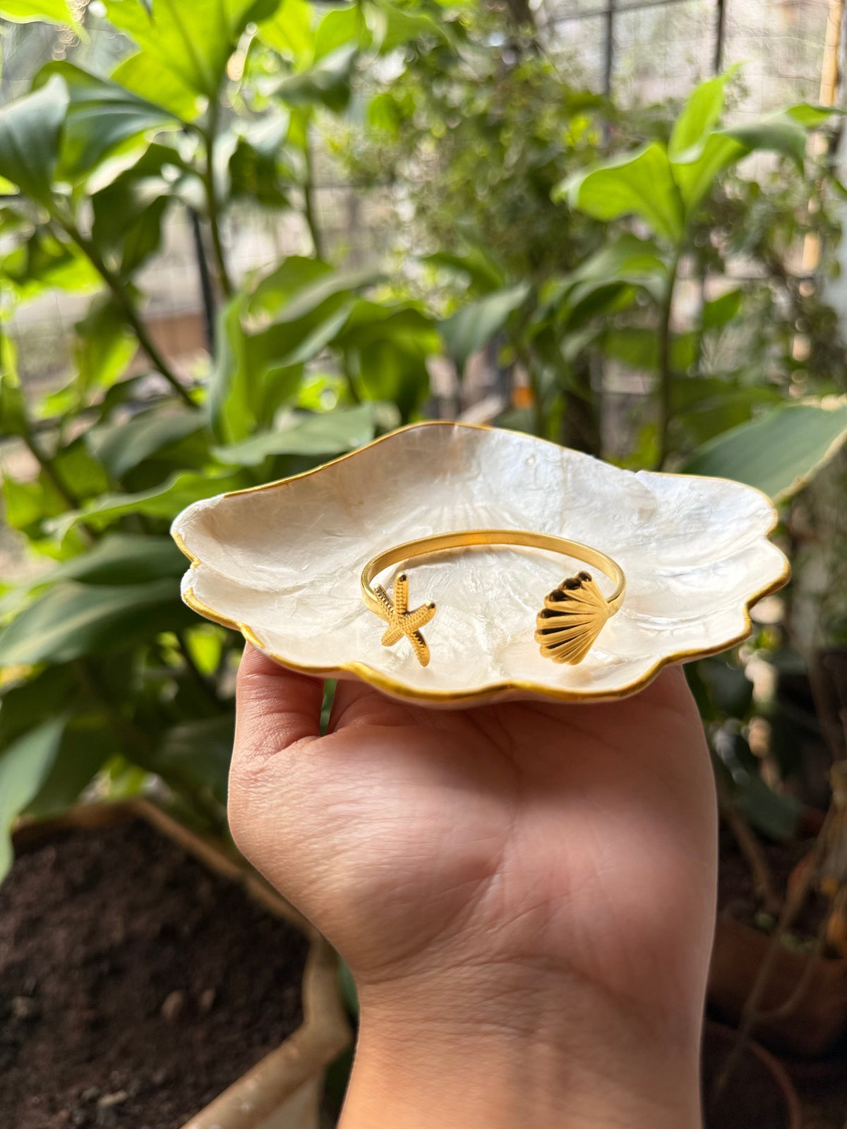 Daga-accessories gold cuff bracelet featuring a starfish and seashell design, held in a shell-shaped dish.