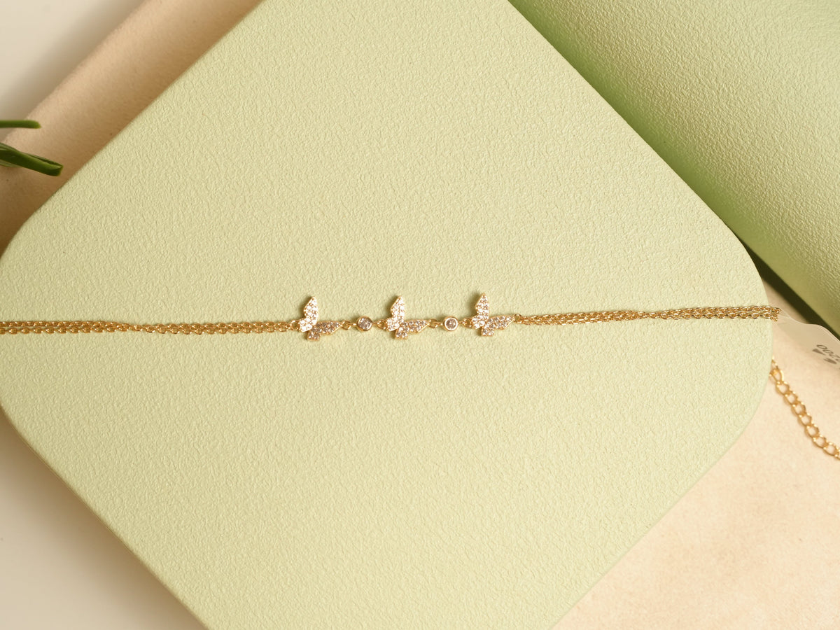 Daga-accessories gold triple butterfly bracelet with delicate crystal accents on a light green textured display base.