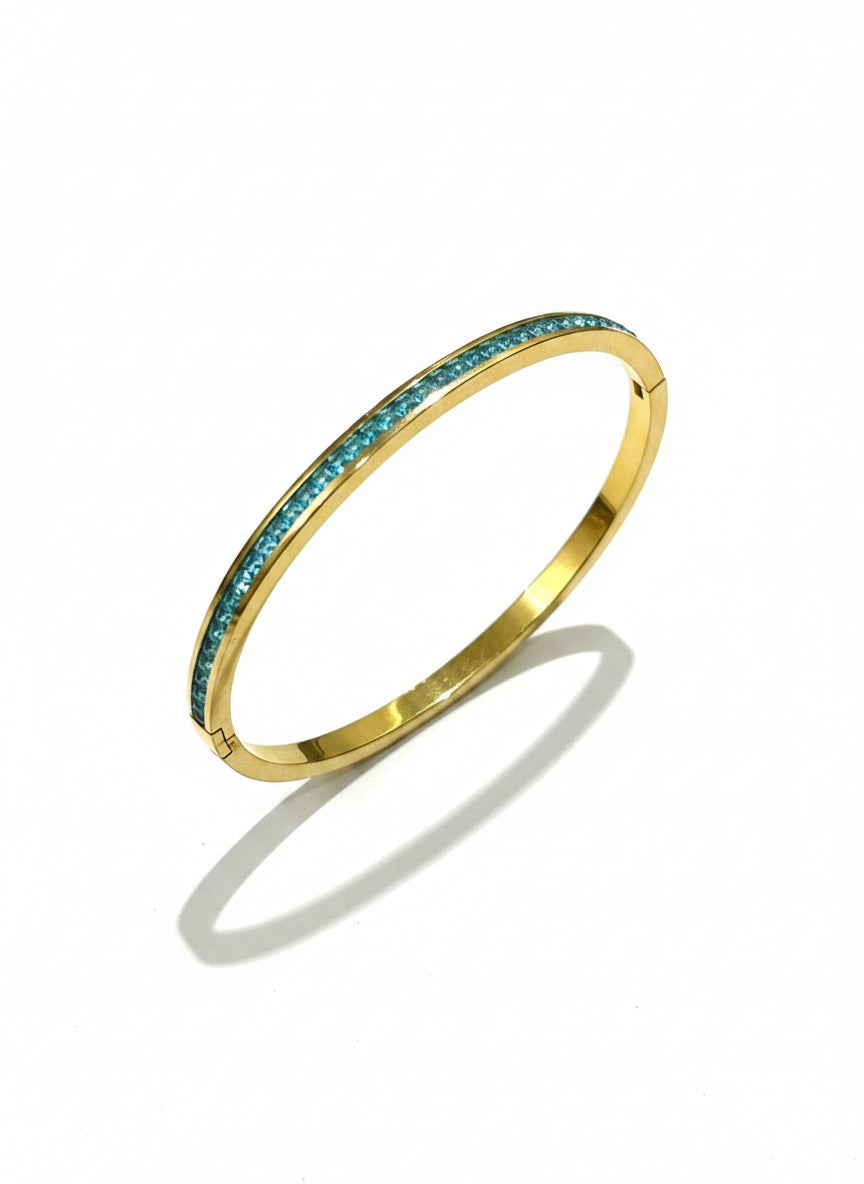 Daga-accessories gold-toned metal bangle bracelet featuring a row of vibrant turquoise-blue crystals and hinged clasp