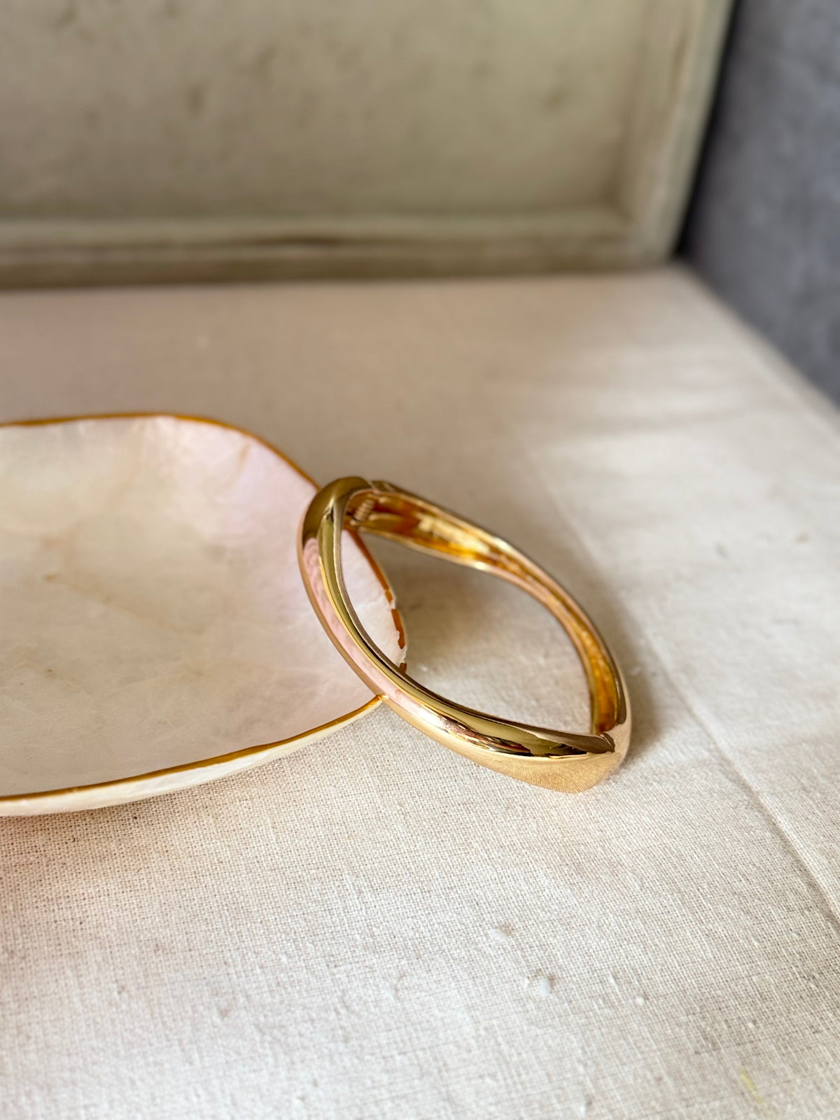 Daga-accessories gold-toned wavy cuff bracelet with a high-shine glossy finish resting on a decorative dish.