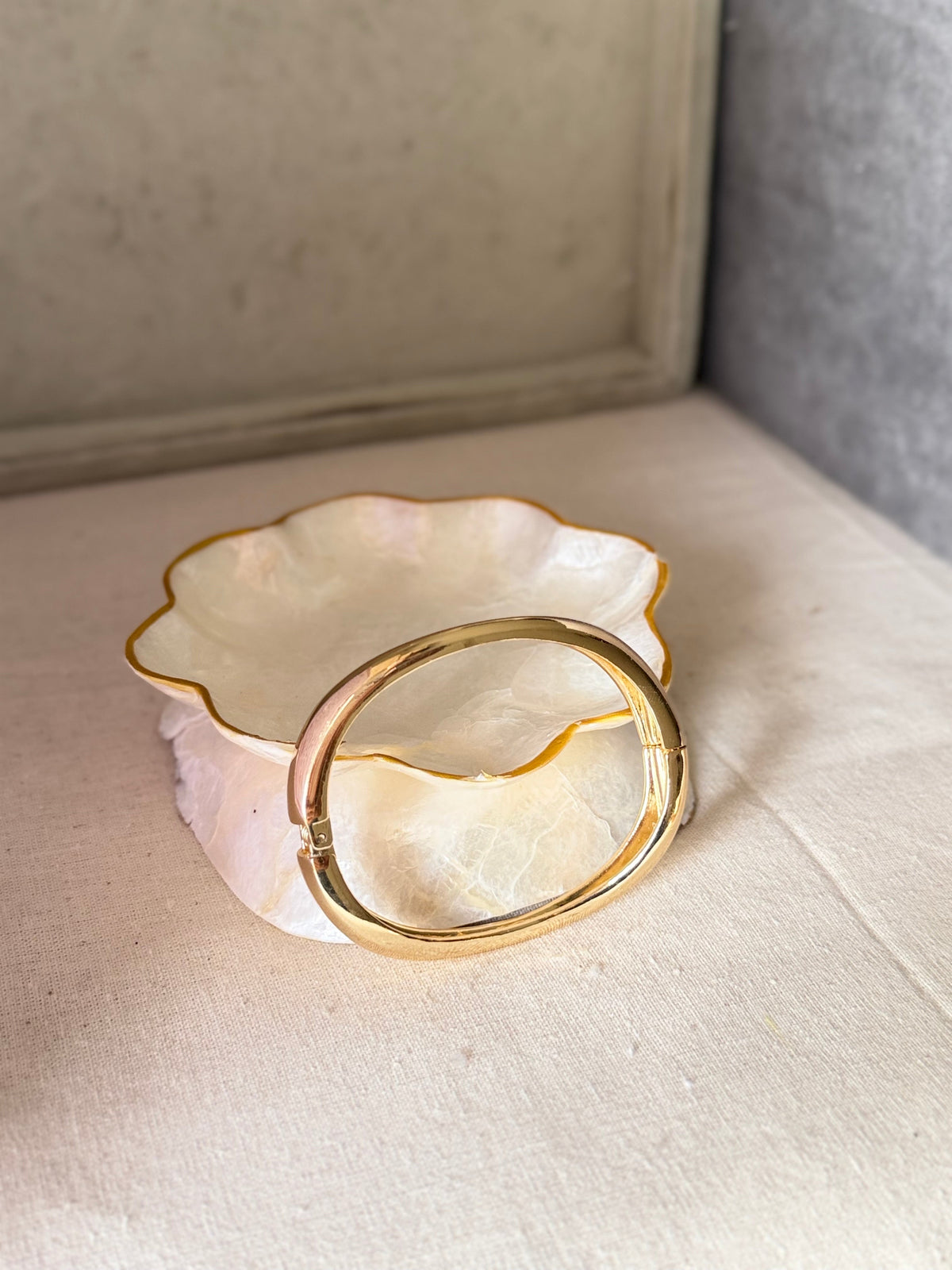Daga-accessories gold-toned wavy cuff bracelet with a high-shine glossy finish resting on a decorative shell dish.