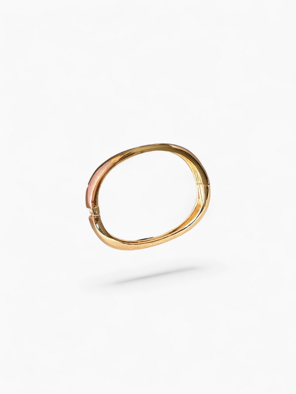 Daga-accessories gold-tone hinged bangle bracelet with a wavy silhouette resting on a decorative shell dish