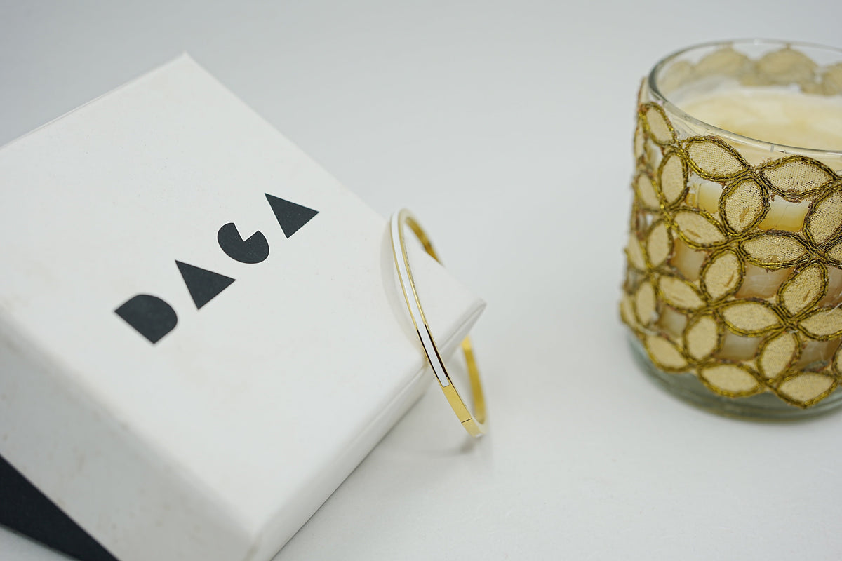 Daga-accessories minimalist gold-tone bangle bracelet with a sleek white enamel inlay resting on a branded gift box.