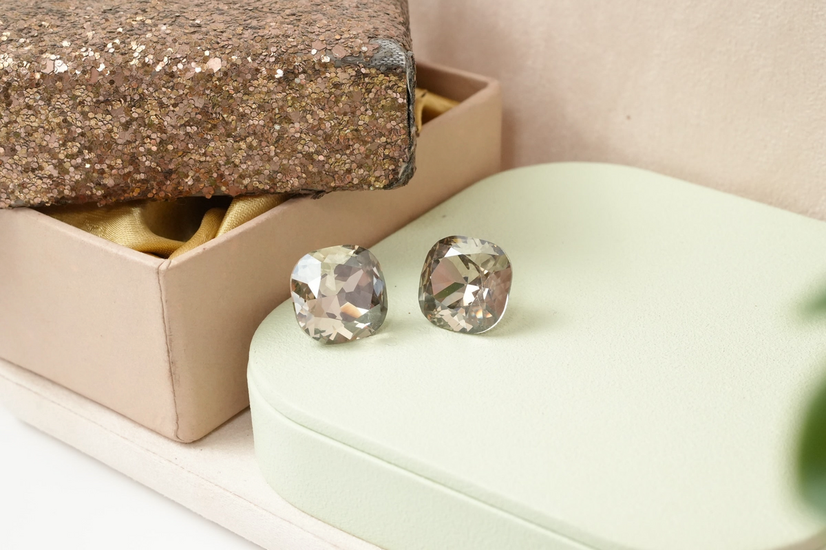 Daga-accessories cushion-cut grey crystal stud earrings with a rounded square silhouette on a light green display