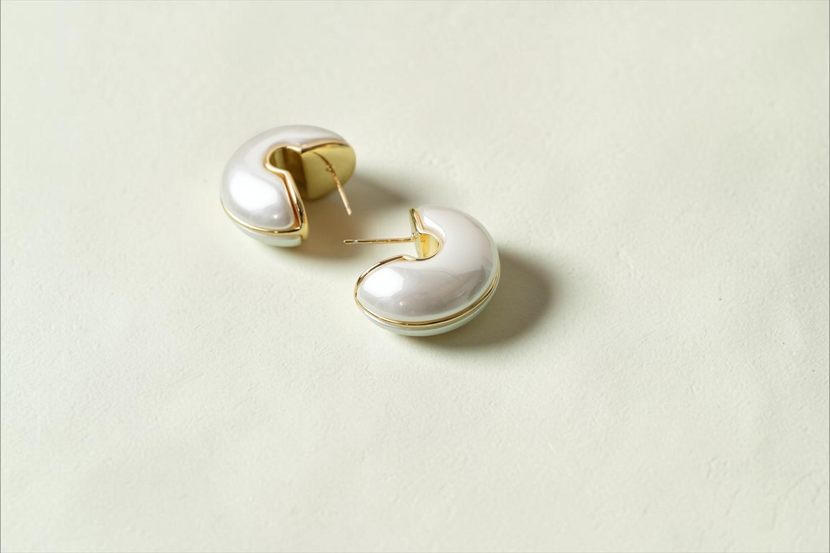 Daga-accessories half moon hoop earrings with a lustrous white finish and gold-toned metallic edges on a green base.
