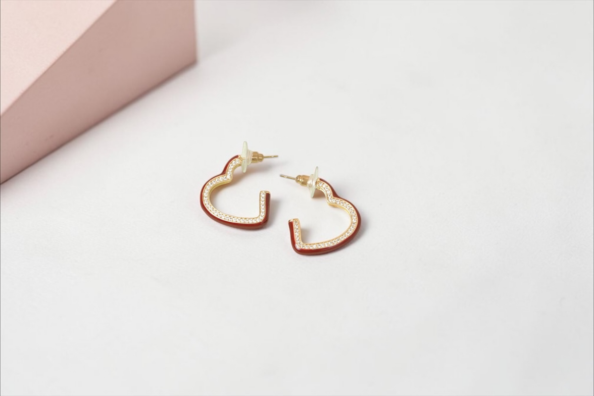 Daga-accessories heart-shaped hoop earrings with red enamel and pave-set stones on a gold-tone finish.