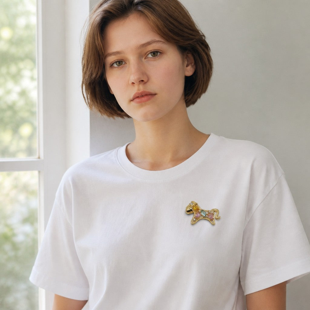 Daga-accessories gold-tone horse brooch with multi-colored crystals pinned to a woman wearing a white t-shirt