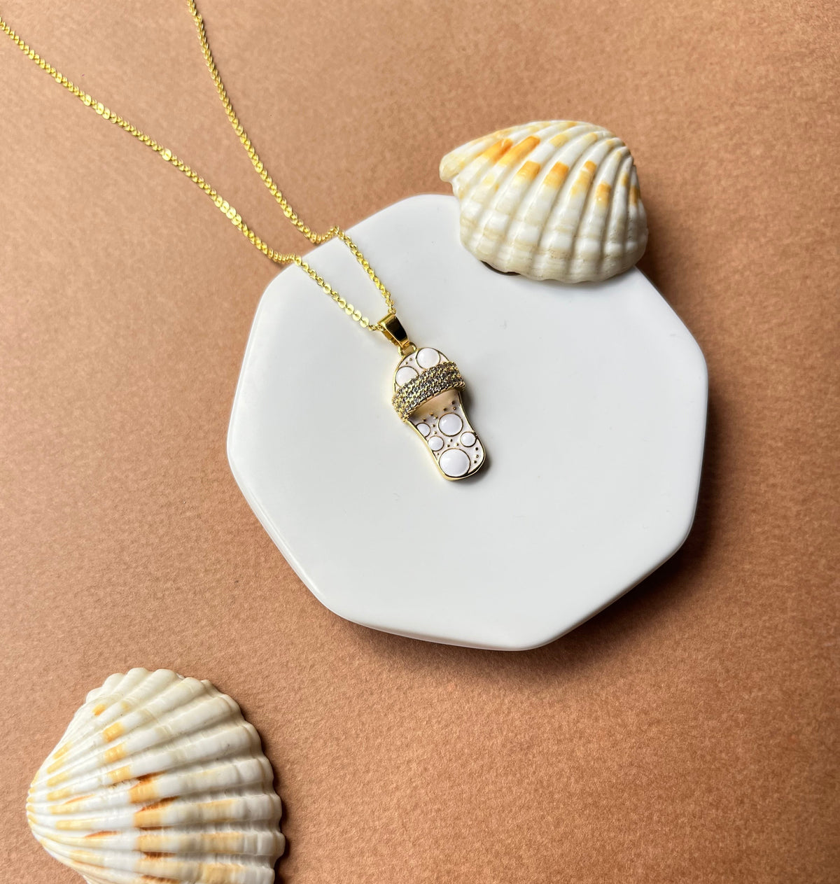 Daga-accessories ivory sandal pendant necklace with gold chain and crystal accents on a white hexagonal display