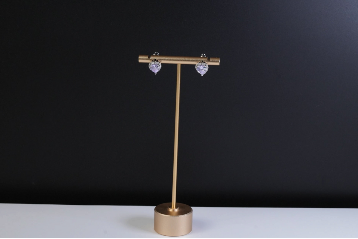 Daga-accessories heart-shaped stud earrings with lavender stones and white crystal halos on a gold display stand
