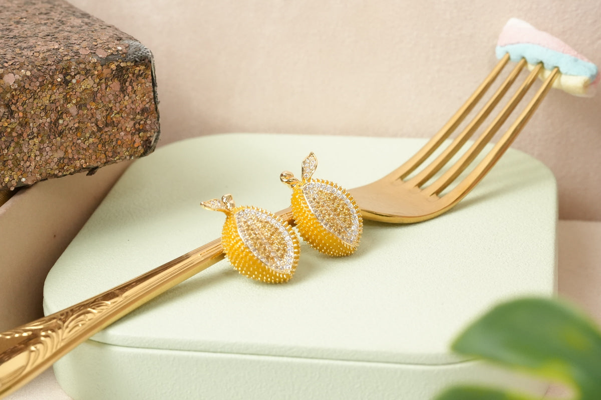 Daga-accessories lemon-shaped stud earrings with yellow textured finish and sparkling cubic zirconia on a gold fork.