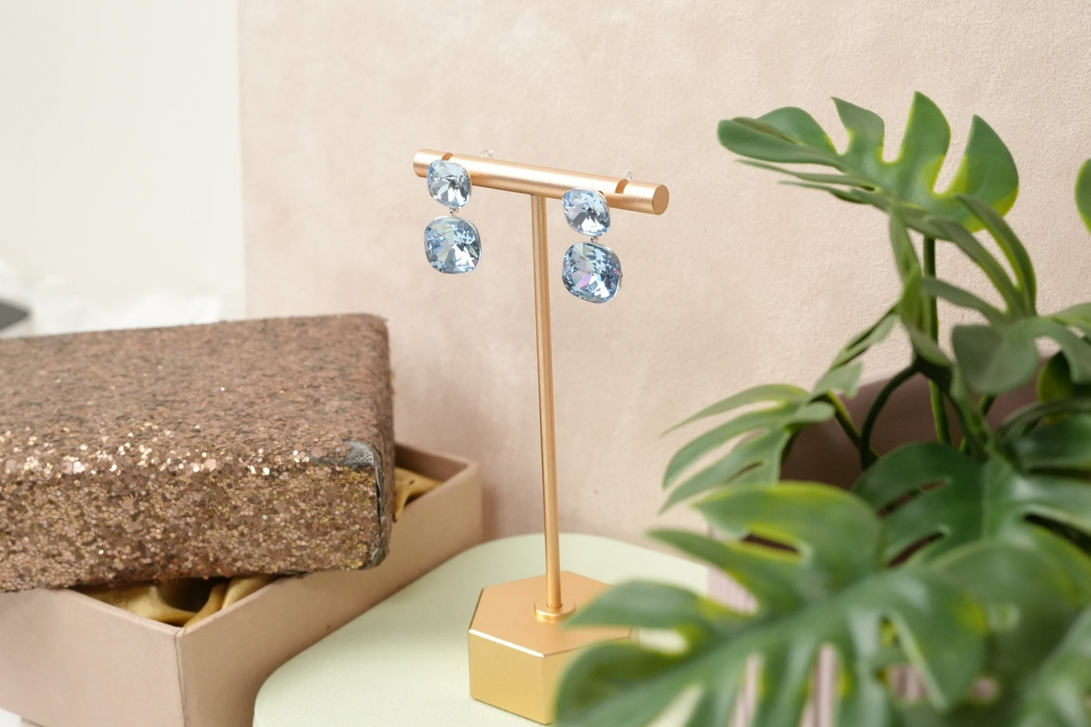 Daga-accessories double-drop earrings featuring faceted light-blue crystals on a gold display stand