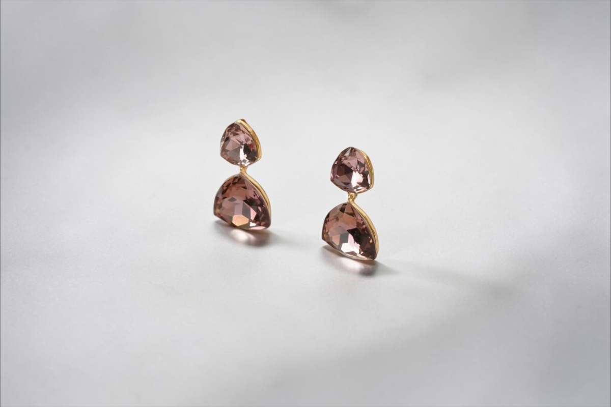 Daga-accessories double-drop geometric earrings with mauve crystals in a polished gold-tone setting on a display stand.