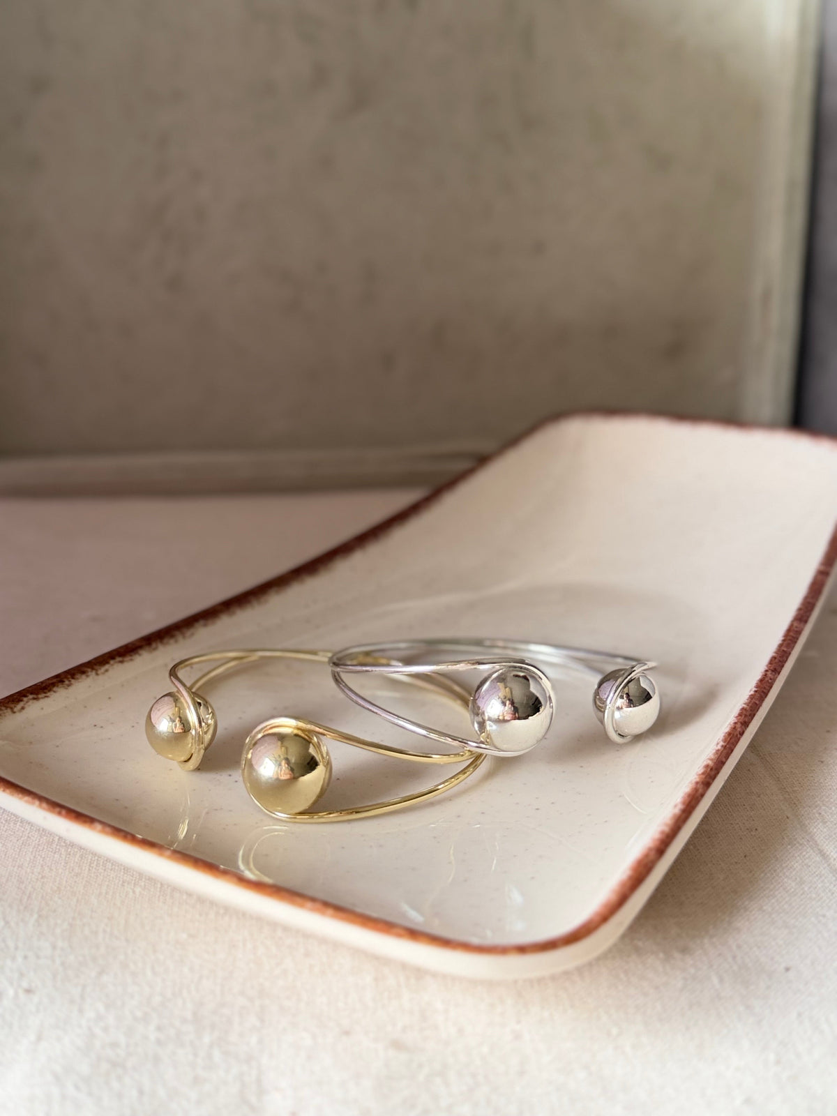 Daga-accessories open cuff bracelets featuring polished silver and gold spherical ends on a ceramic tray
