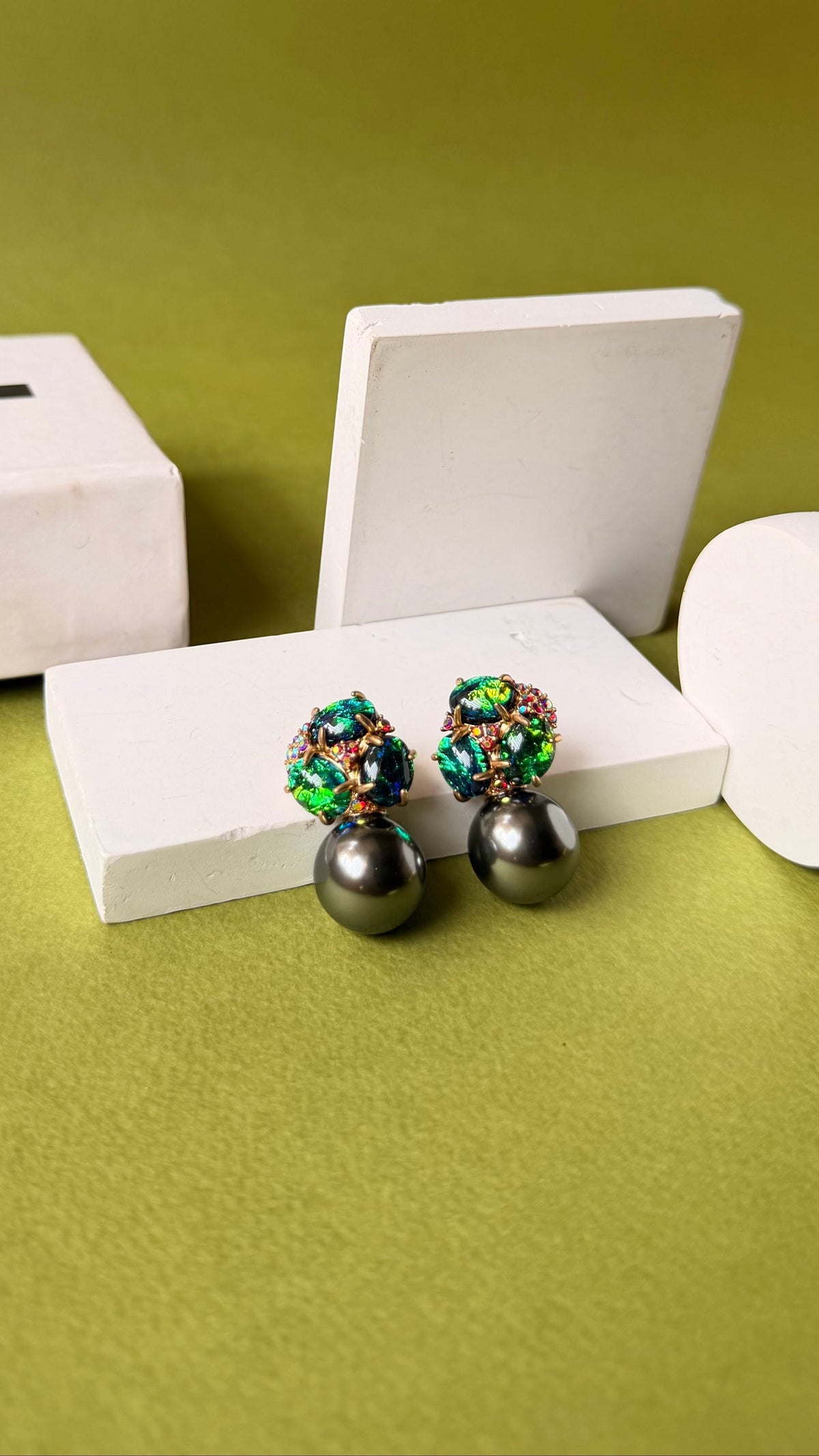 Daga-accessories Midnight edit earrings with green crystal petal clusters and dark grey pearl drops on a green base.