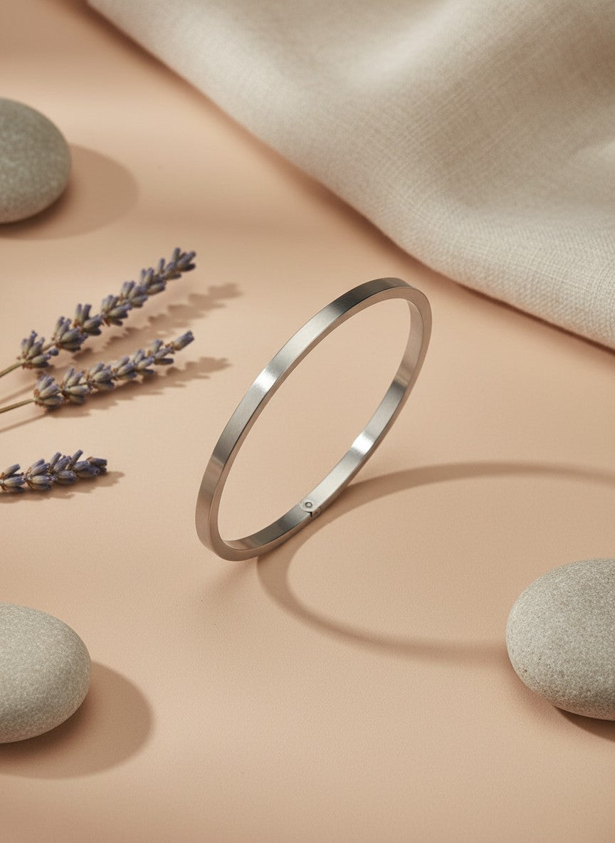 Daga-accessories minimalist silver-tone stainless steel bangle bracelet on a beige surface with stones and lavender.