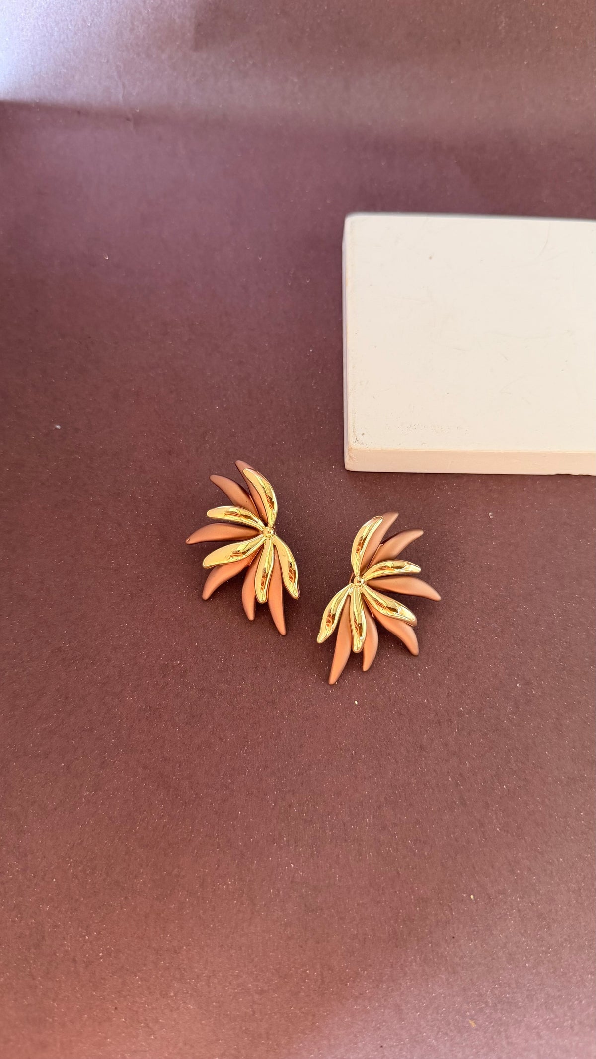 Daga-accessories gold-toned statement earrings with mocha petal-inspired accents on a brown background
