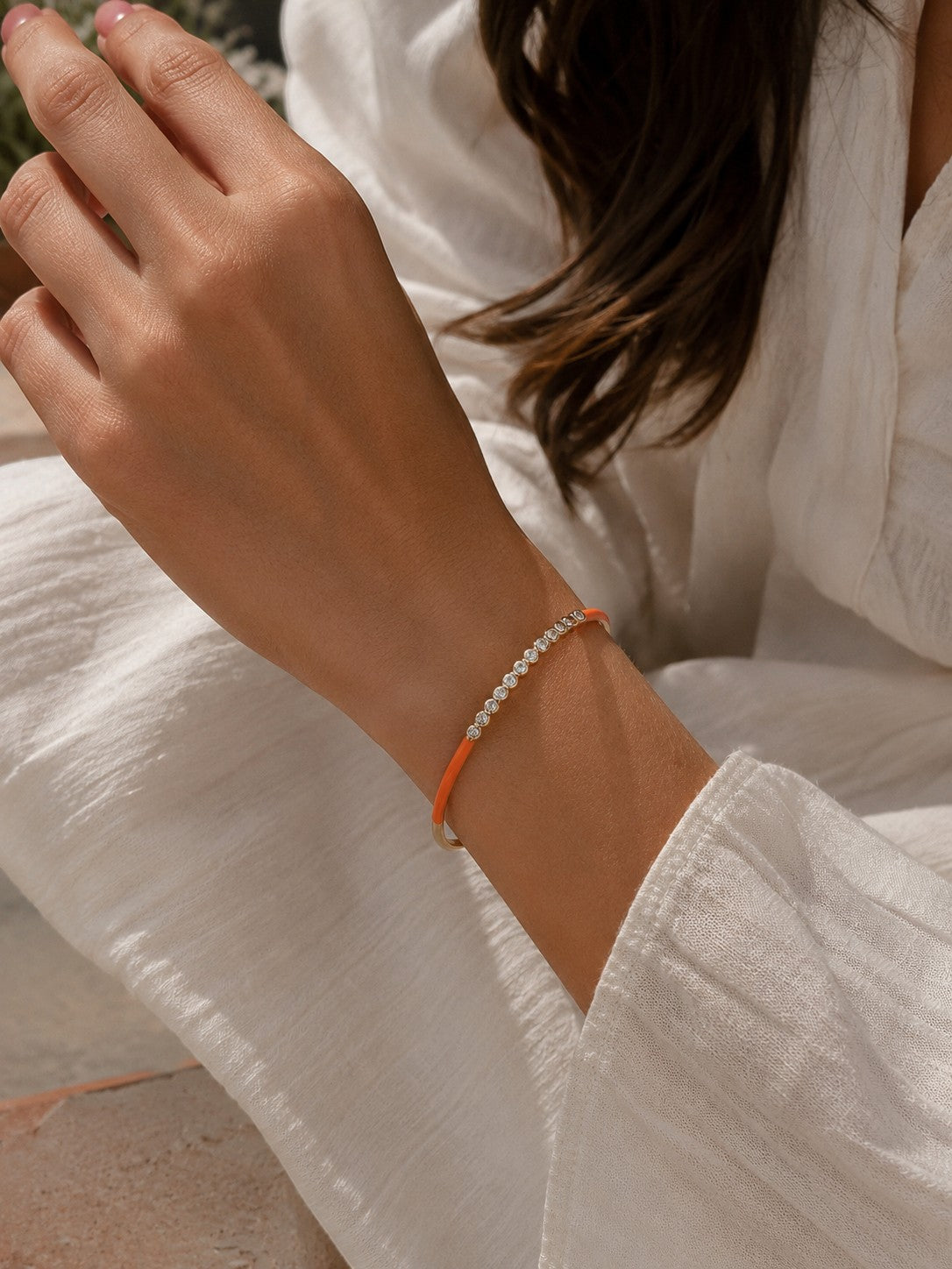 Daga-accessories orange enamel bracelet with a row of sparkling crystals worn on a woman's wrist