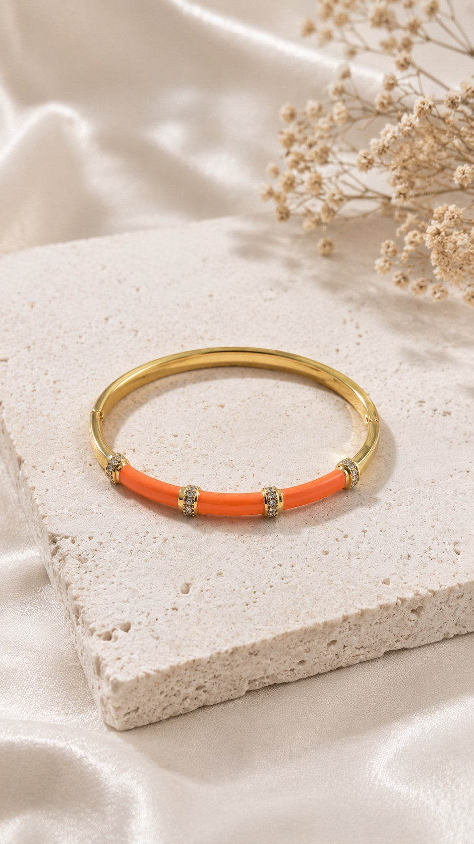 Daga-accessories orange enamel bar bracelet with gold-tone metal and sparkling crystal accents on a stone display