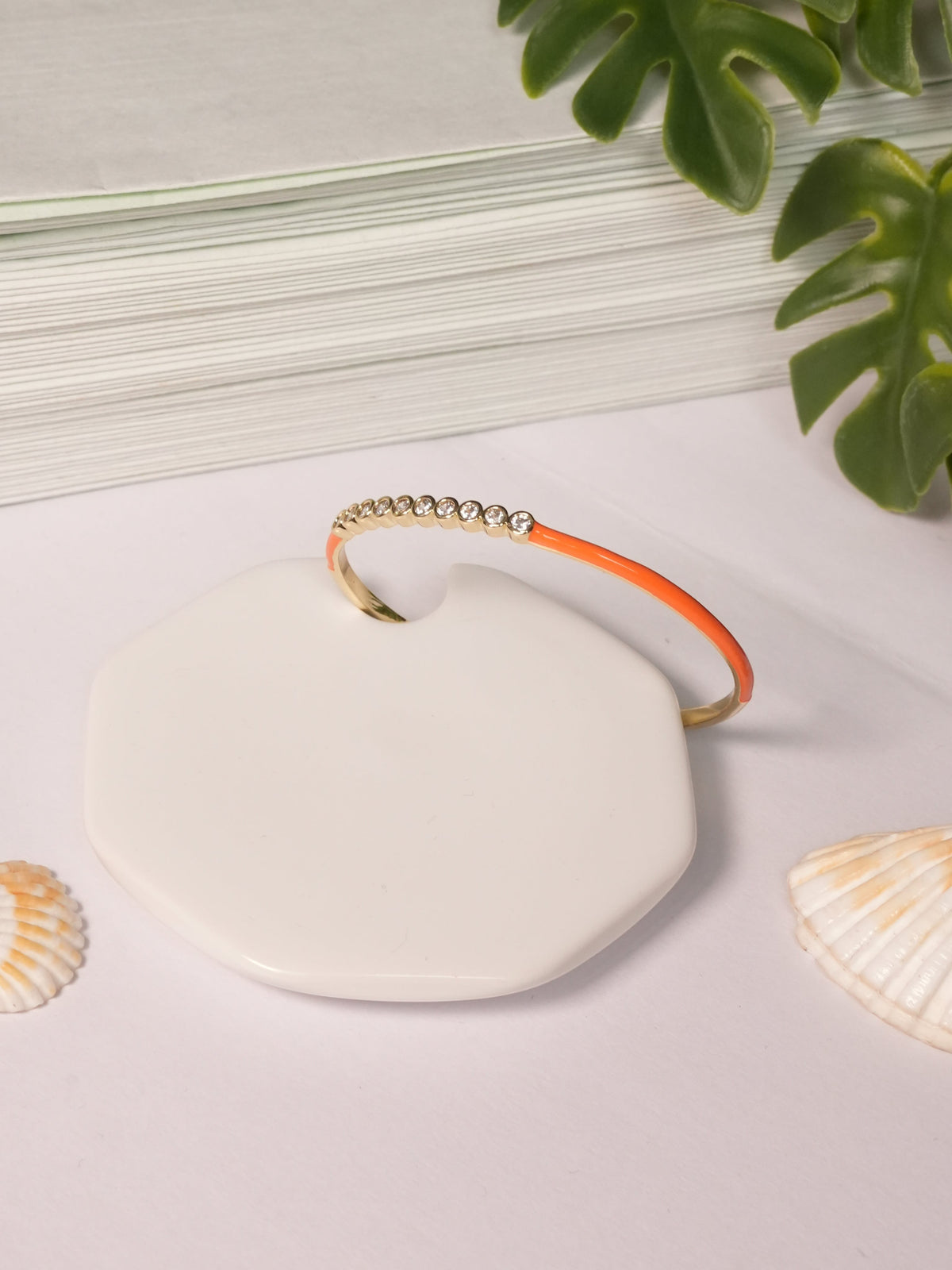 Daga-accessories orange enamel bracelet with a row of sparkling crystals on a white display stand