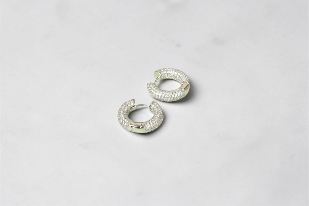 Daga-accessories silver-tone chunky hoop earrings with pavé cubic zirconia stones on a light green display stand.