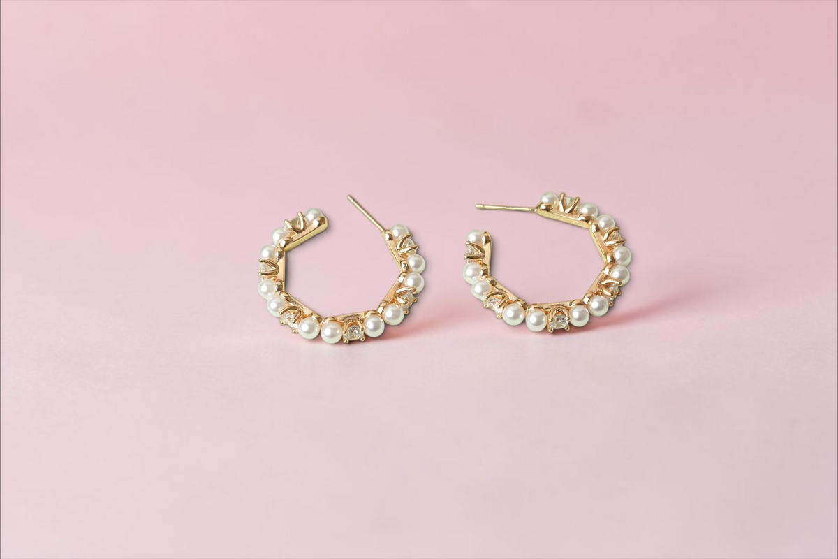Daga-accessories gold-tone hoop earrings featuring alternating faux pearls and clear crystals on a green display base.