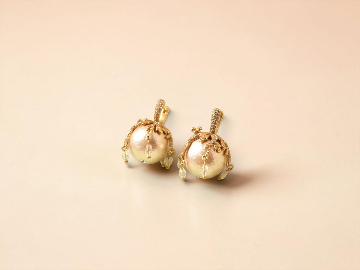 Daga-accessories elegant pearl drop earrings with gold-toned botanical accents and stone-studded clasps on a green base.