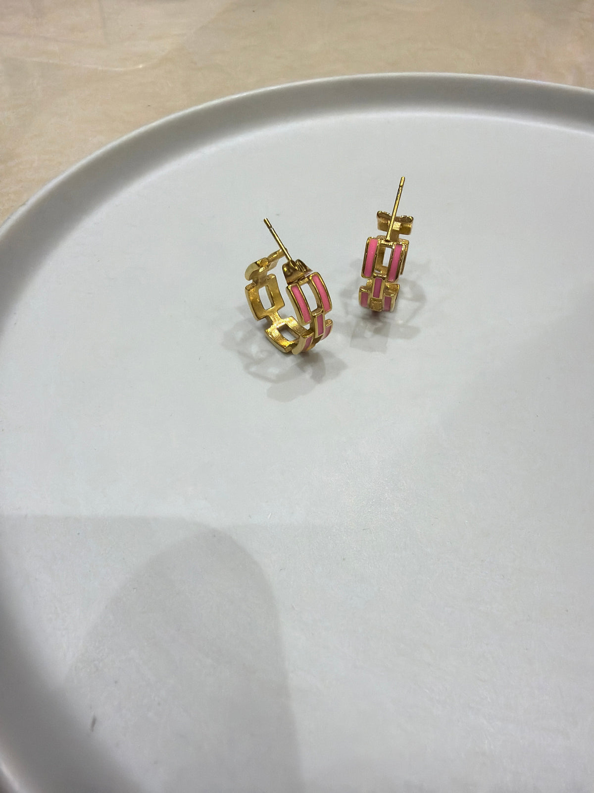 Daga-accessories gold hoop earrings featuring a pink enamel chain-link design on a white ceramic plate