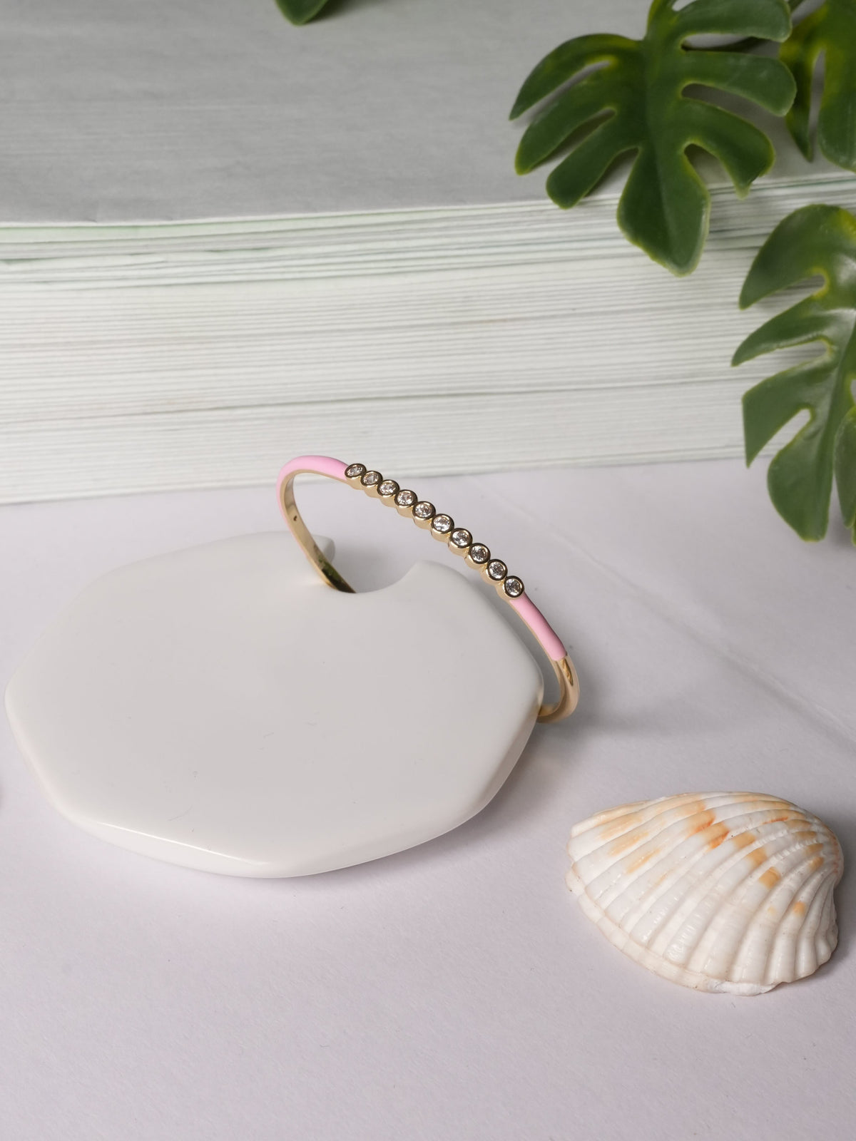 Daga-accessories pink enamel bangle bracelet with a row of sparkling crystal accents on a white display stand.