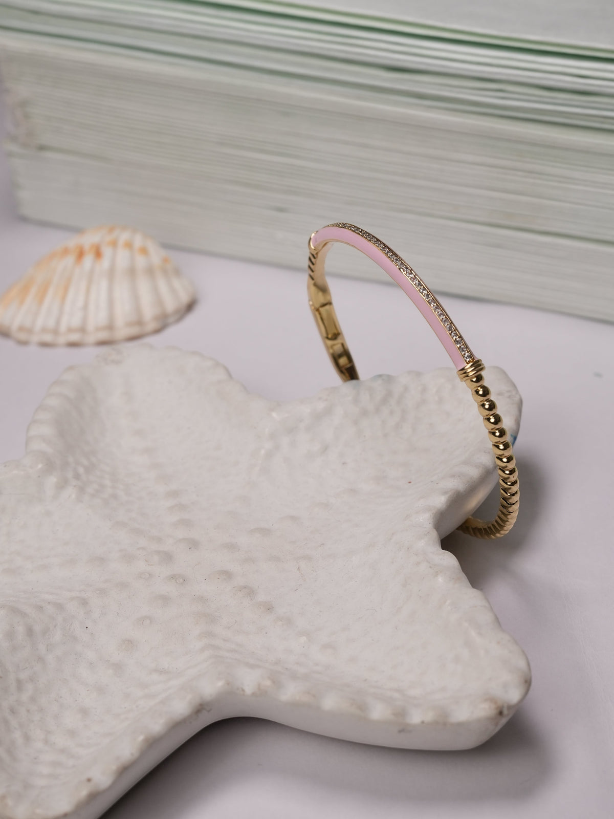 Daga-accessories baby pink enamel slim aura bracelet with gold-tone beaded detailing resting on a starfish dish