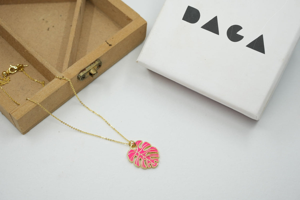 Daga-accessories gold chain necklace featuring a vibrant pink monstera leaf pendant, presented in a gift box.