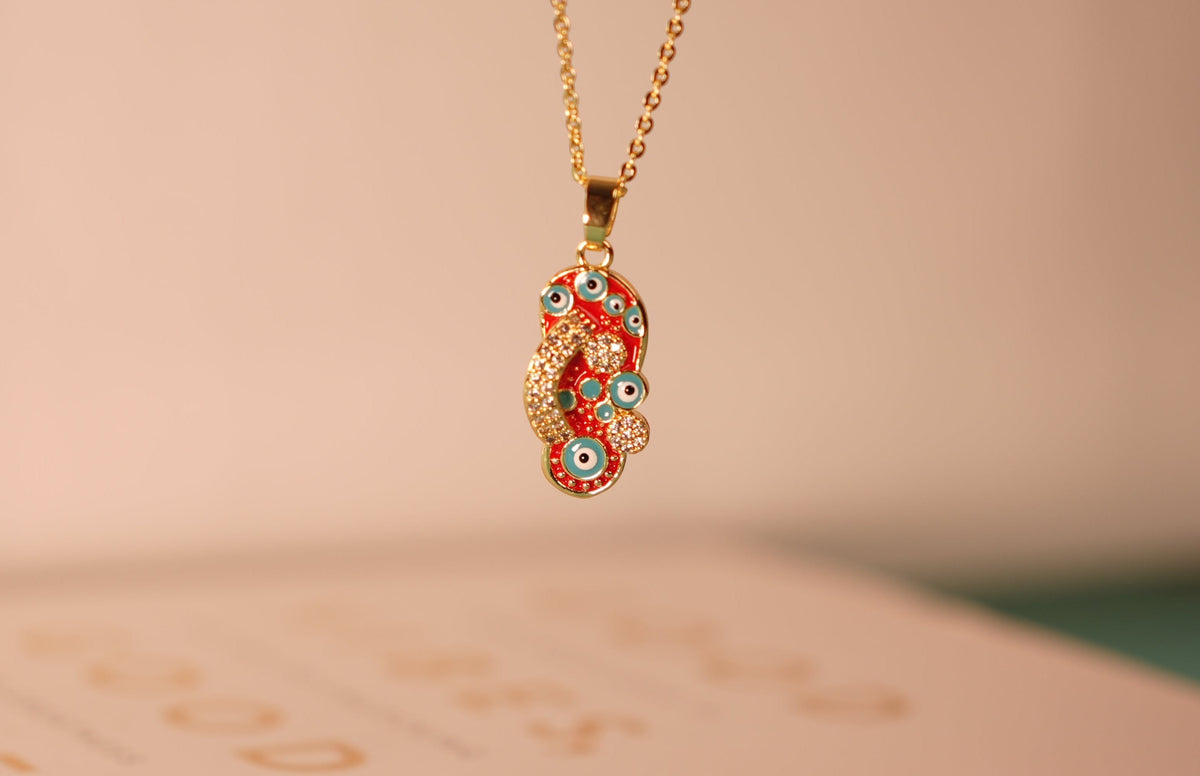 Daga-accessories Starry Steps red necklace featuring a gold chain and a flip-flop pendant with evil eye motifs.