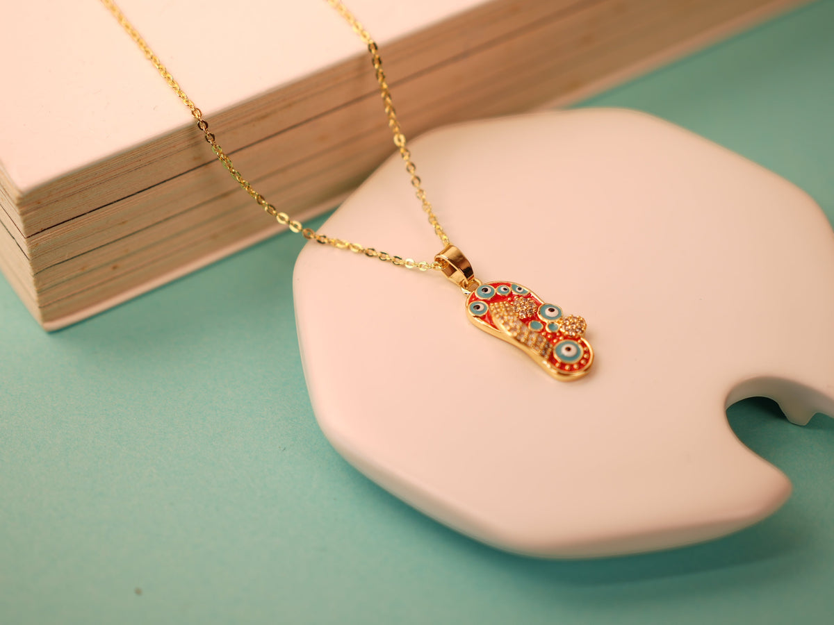 Daga-accessories Starry Steps red necklace featuring a gold chain and a foot-shaped pendant with blue evil eye accents