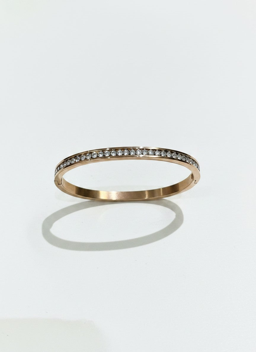 Daga-accessories rose gold-toned bangle bracelet featuring a row of shimmering crystals and a polished finish.