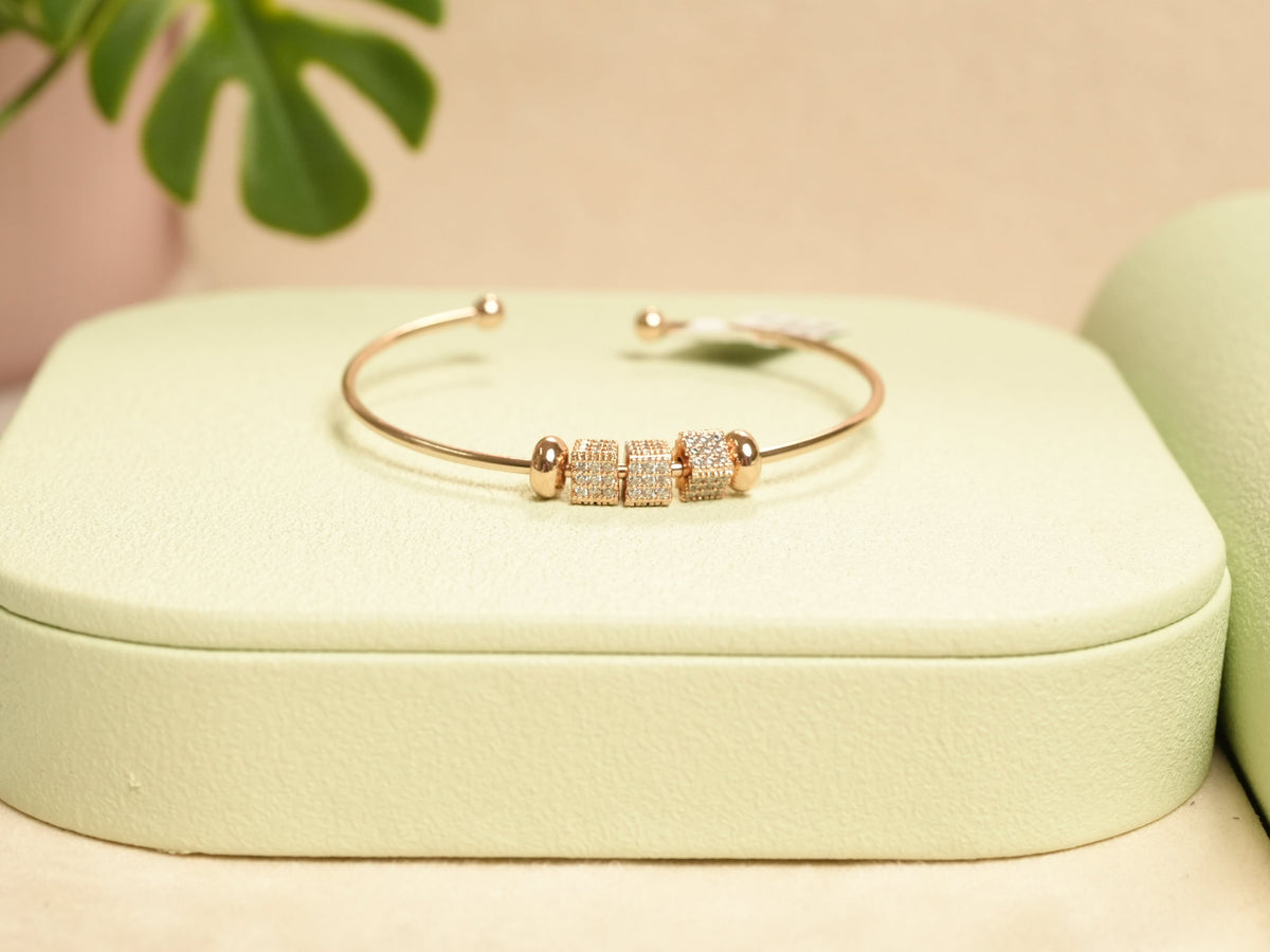Daga-accessories rose gold bangle bracelet with three cubic zirconia encrusted cube beads on a light green display
