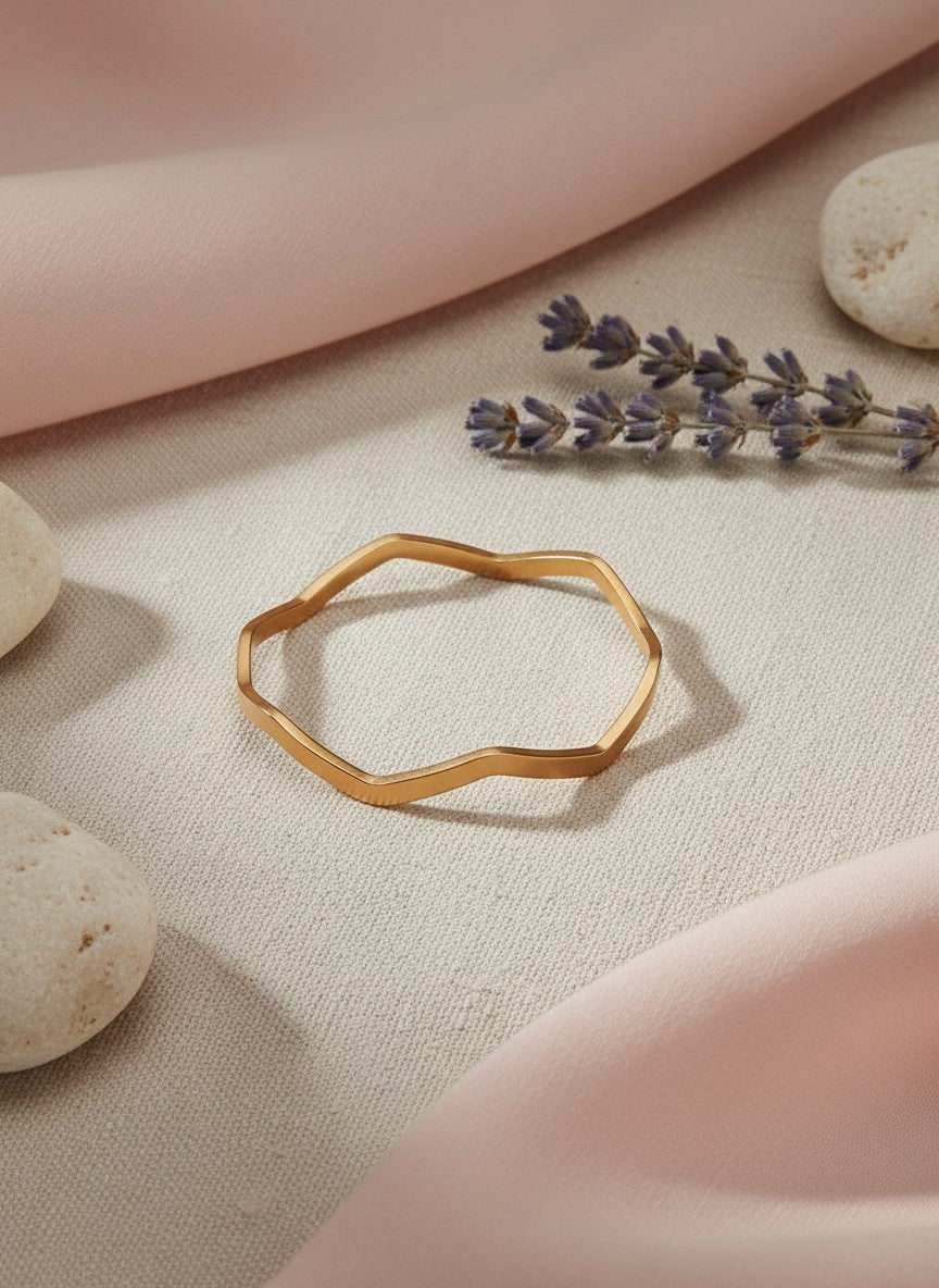 Daga-accessories rose gold-toned geometric wave bangle with a polished finish on a soft fabric background