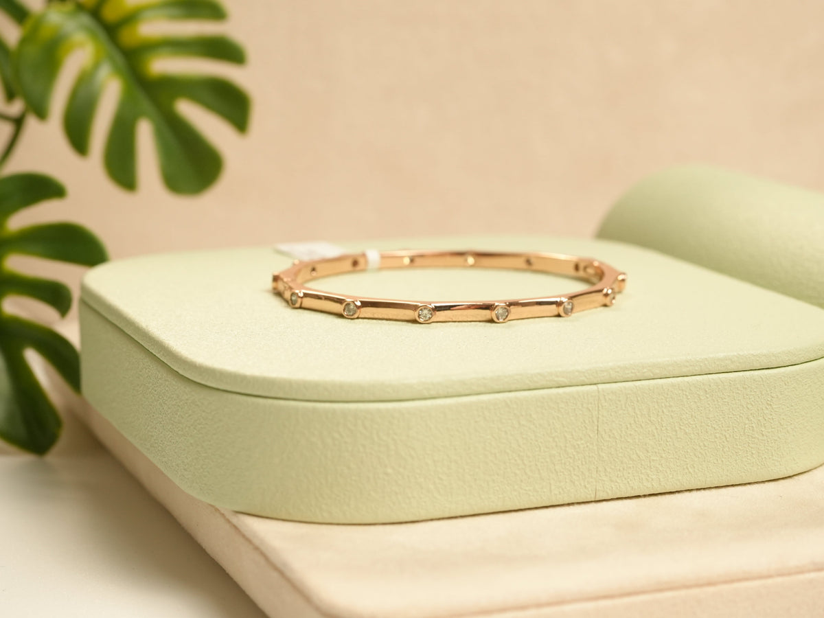 Daga-accessories rose gold hexagon bangle bracelet with inlaid diamonds resting on a soft green display stand