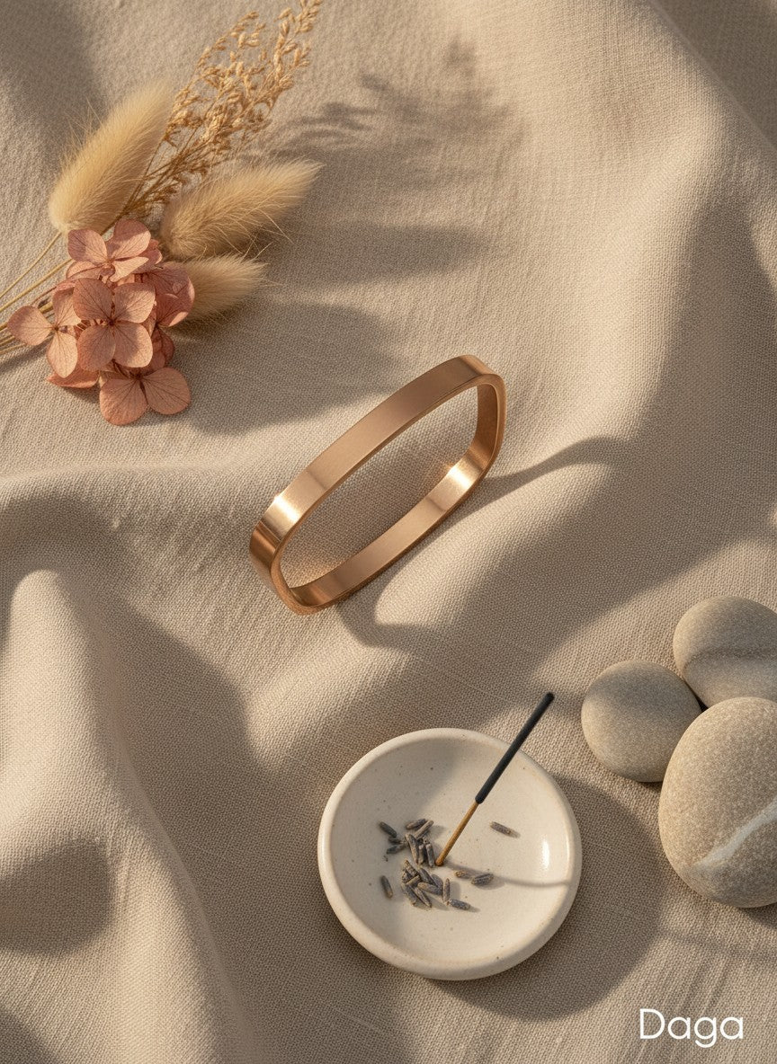 Daga-accessories minimalist rose gold-toned rectangular bangle bracelet with a polished finish on beige linen fabric.