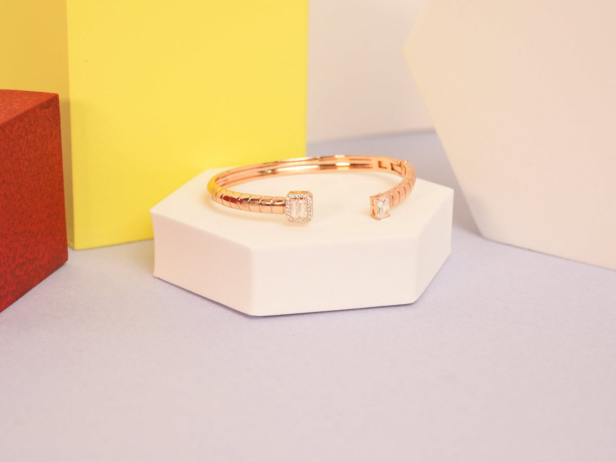 Daga-accessories rose gold cuff bracelet with a minimal solitaire emerald-cut stone on a white hexagonal pedestal.